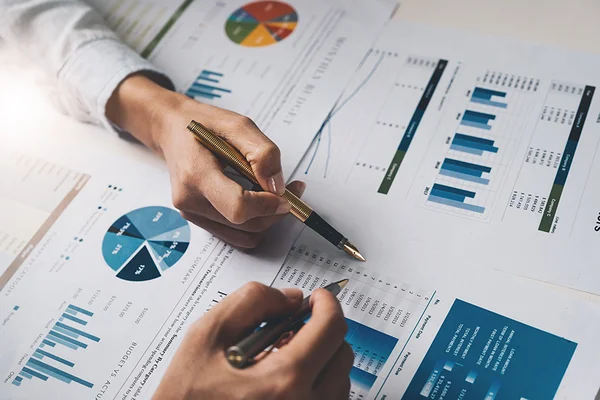 hands holding pens pointing to financial graphs